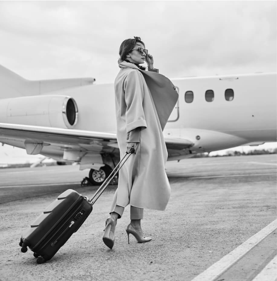 Black and white image of woman walking to a private plane with luggage
